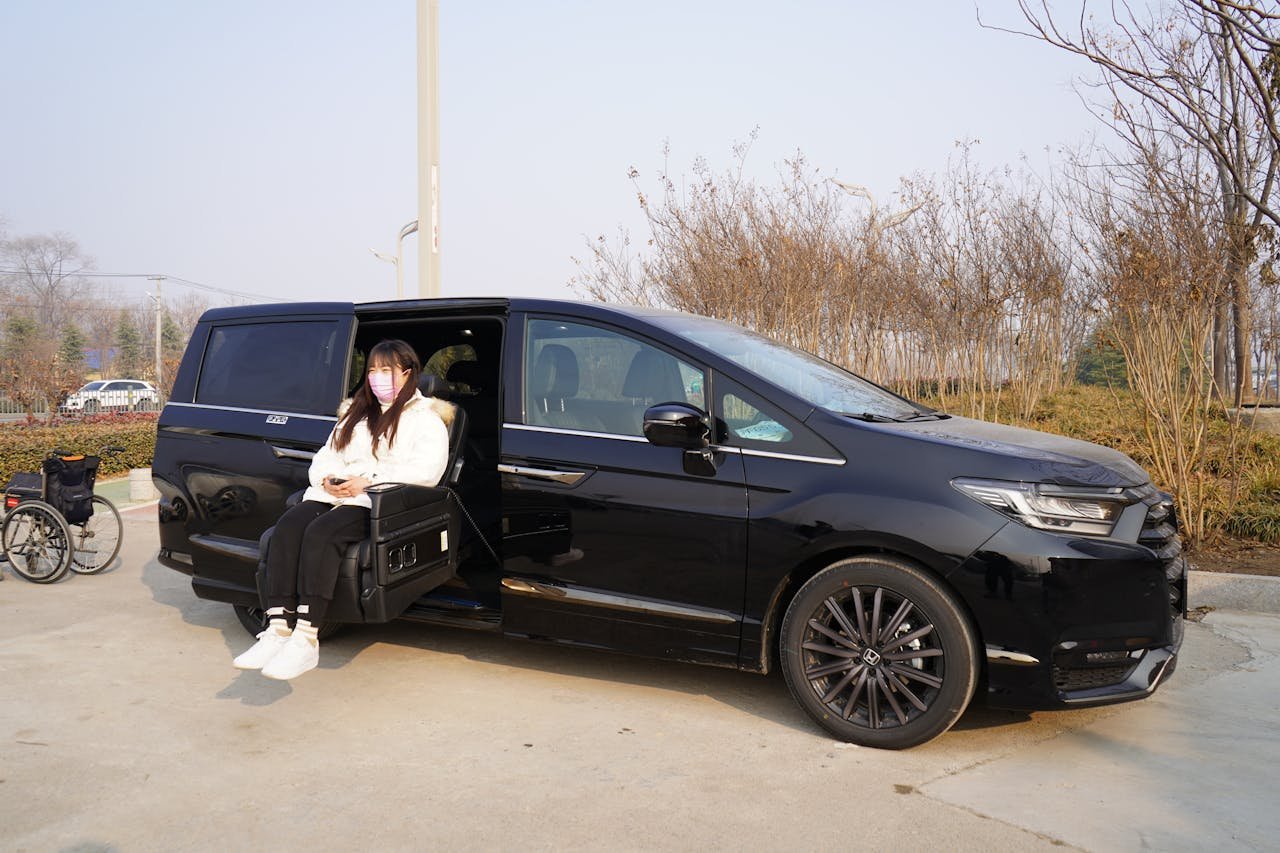 Woman in face mask using sliding seat in black car with nearby wheelchair.