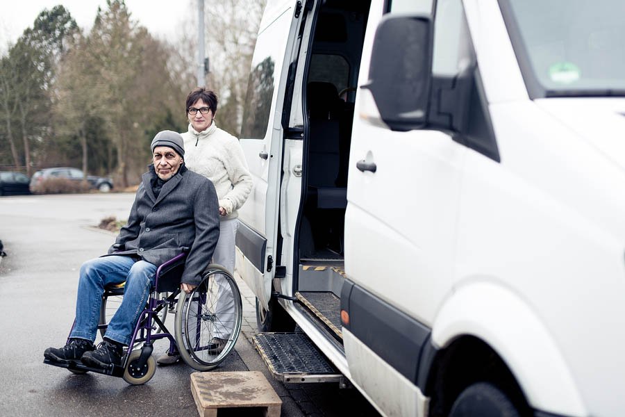 nurse helping senior man exit a van and get to his wheelchair